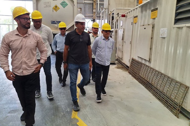 Foto mostra homens com capacete na cabeça andando numa empresa