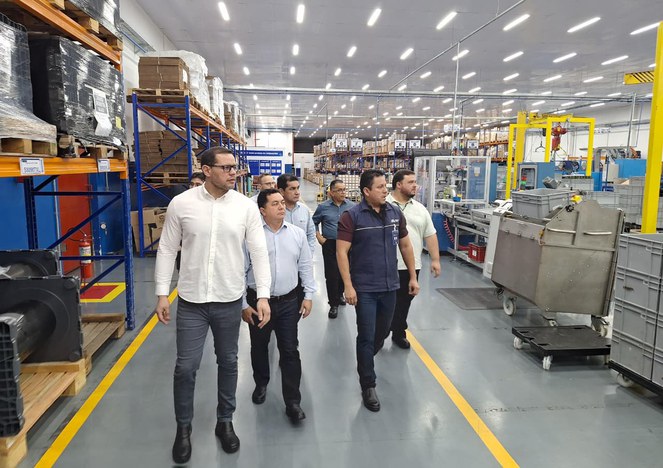 Foto mostra homens caminhando dentro de uma fábrica