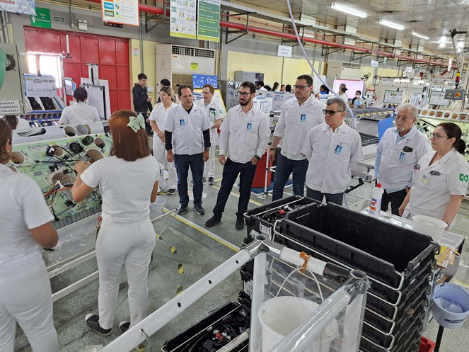 Foto mostra grupo de pessoas vestidas com roupas brancas dentro de uma fábrica