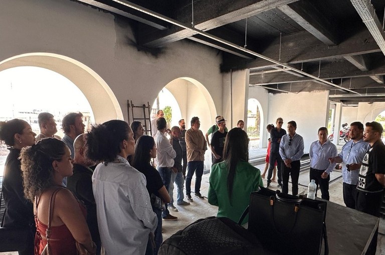 Foto mostra homem falando, observado por um grupo de pessoas