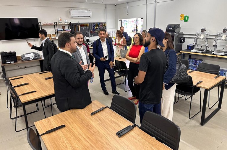 Foto mostra homem de blazer escuro falando a pessoas dentro de uma sala de pesquisa
