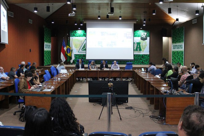 Foto mostra pessoas reunidas num auditório com um grande painel ao fundo