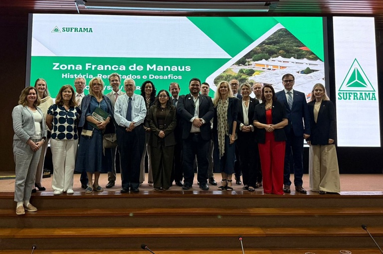 Foto mostra pessoas posanto para sessão de foto tendo um telão iluminado ao fundo