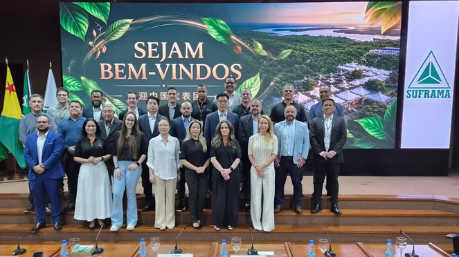 Foto mostra pessoas reunidas para sessão de foto num auditório, com o apoio de um telão