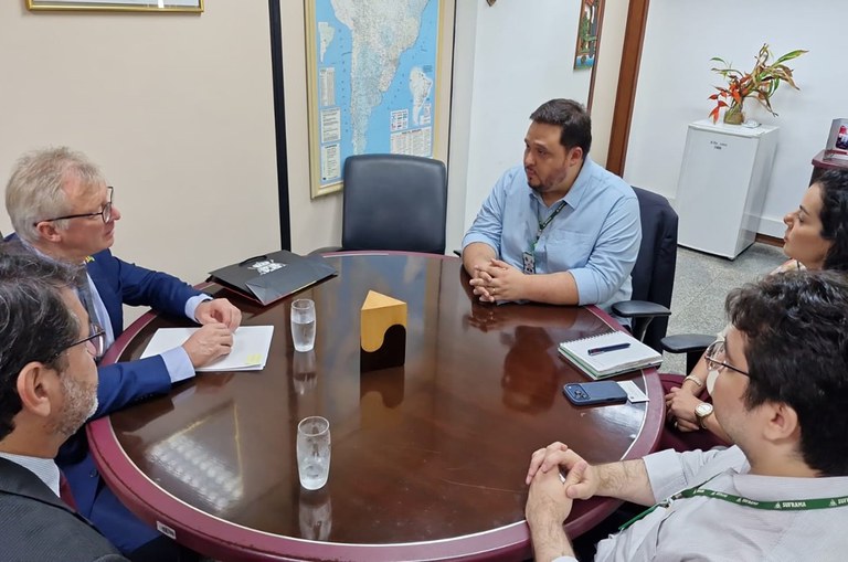 Foto mostra homem de blusa azul clara falando a outro homem vestido de blazer azul escuro