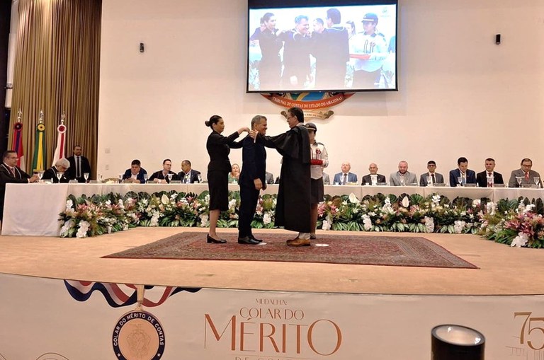 Foto mostra homem recebendo medalha, num auditório lotado