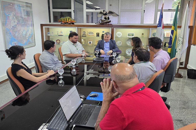 imagem com várias pessoas em reunião ao redor de uma mesa retangular, com o superintendente na ponta da mesa, ao centro da foto