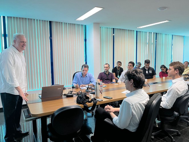 Foto mostra homem de blusa branca falando a um grupo de pessoas
