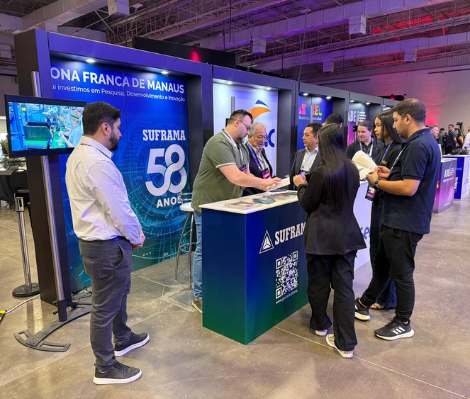 Foto mostra grupo de pessoas e estandes com painéis num grande evento