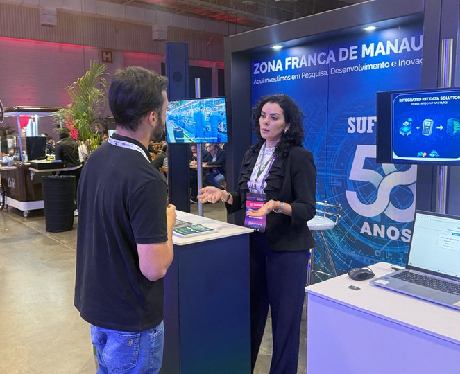 Foto mostra mulher fazendo uma explicação a um homem, com um grande painel ao fundo