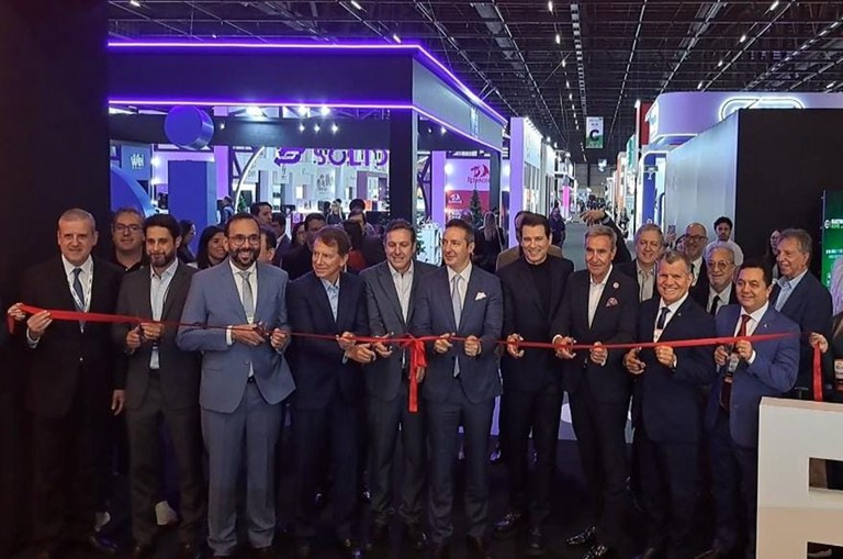 Imagem mostra cerca de 15 homens enfileirados com uma fita a frente para corte simbolizando a abertura da Eletrolar Show