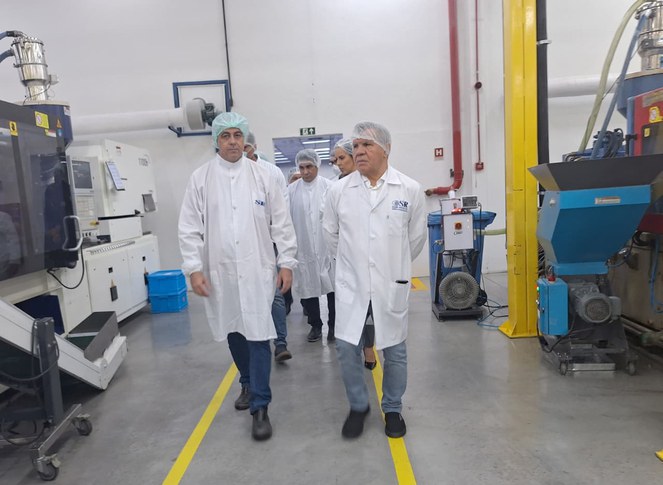 Foto mostra pessoas andando com bata e toucas em uma linha de produção industrial