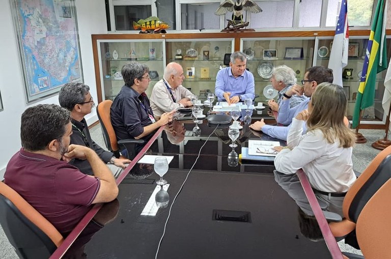 Foto mostra homem ao centro da mesa fazendo uma explicação ao outro homem que está ao lado dele
