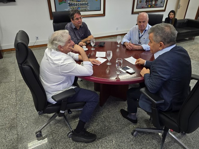 Foto mostra um homem gesticulando em reunião com outros três homens
