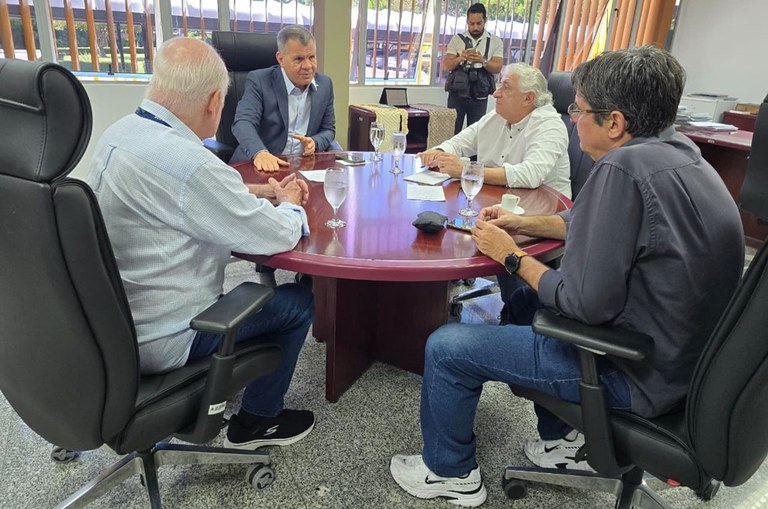 Foto mostra homem gesticulando em reunião com outros três homens