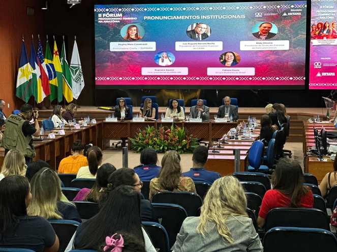 Foto mostra pessoas em evento num auditório, com telão ao fundo