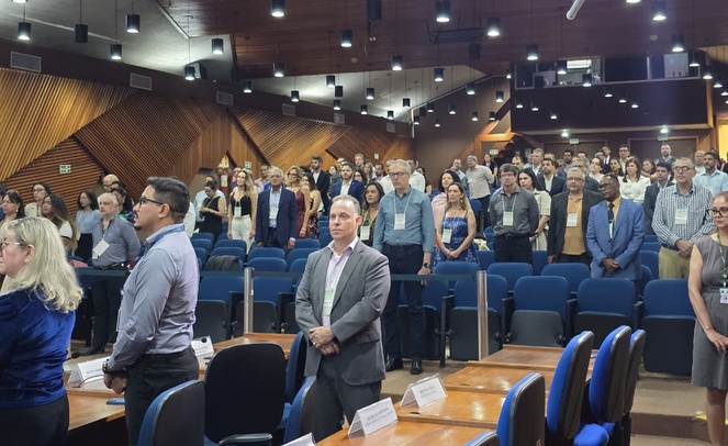 Foto mostra pessoas em pé em um auditório lotado