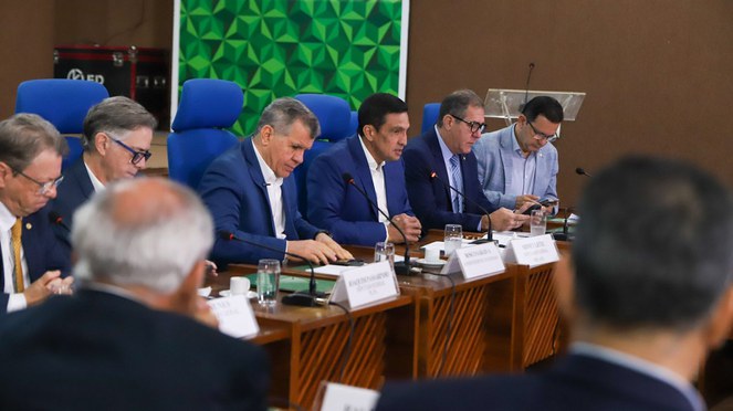 Foto mostra homem de paletó azul falando ao microfone