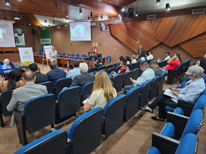 Foto mostra homem em pé de blazer bege falando em público