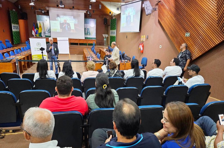 Foto mostra homem falando ao microfone a um grupo de pessoas