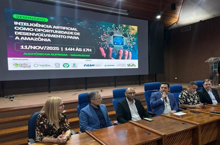 Foto mostra homem de blazer azul falando ao microfone em um evento