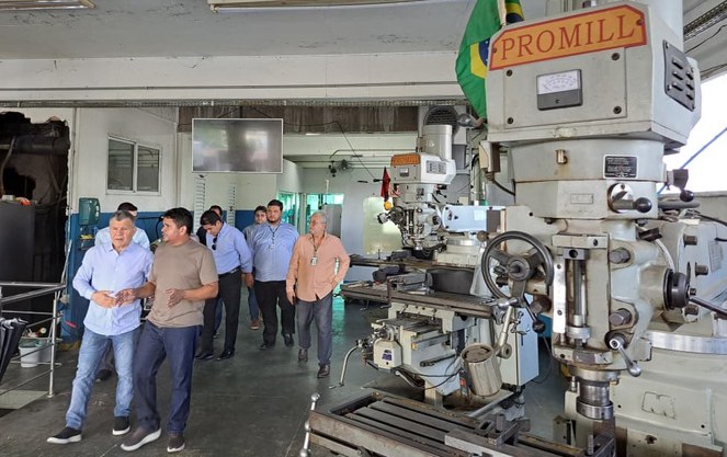 Foto mostra grupo de pessoas andando ao lado de máquinas