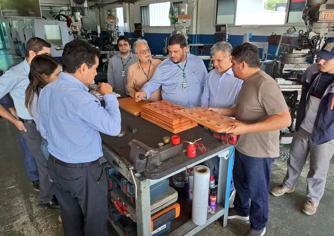 Foto mostra um homem segurando objeto e fazendo uma explicação a grupo de pessoas