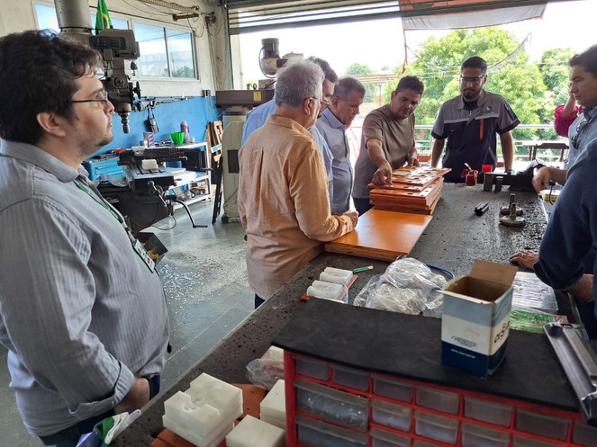 Foto mostra homem segurando um cobjeto e fazendo uma explicação a grupo de pessoas