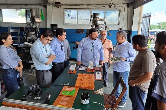 Foto mostra homem segurando objeto, observado por grupo de pessoas