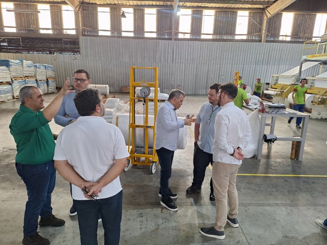 Foto mostra um grupo de pessoas numa fábrica de produtos plásticos