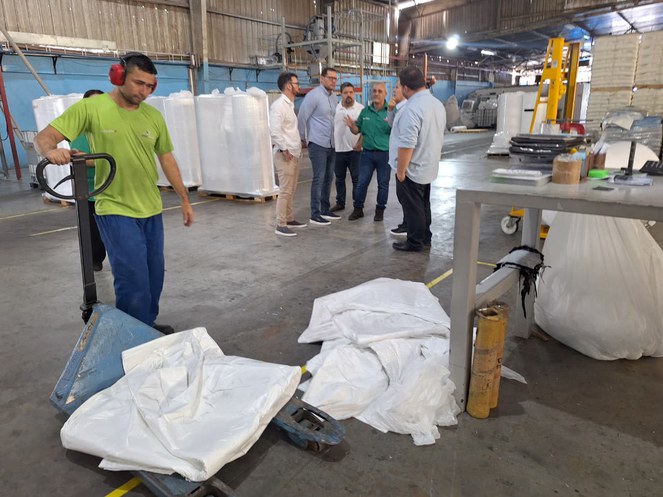 Foto mostra homem mexendo com sacos plásticos e outras pessoas ao fundo conversando