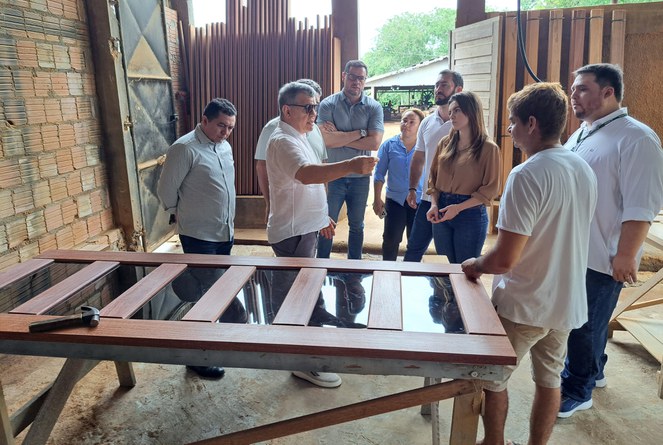 Foto mostra homem de óculos escuro e blusa branca fazendo uma explicação a um grupo de pessoas