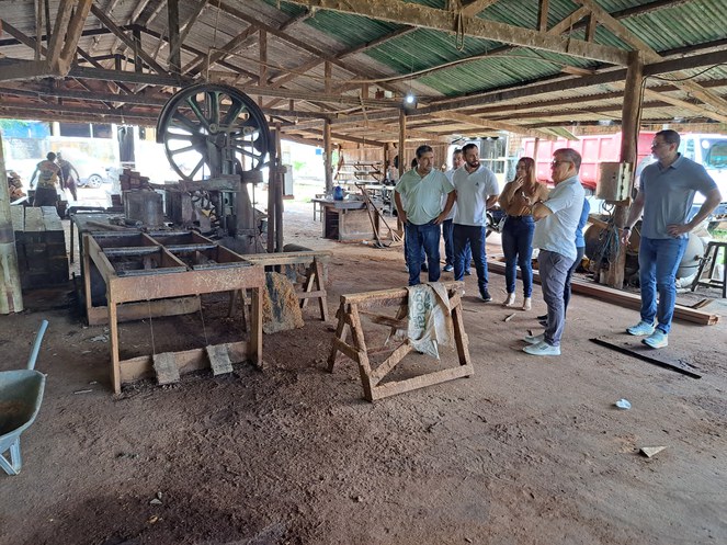 Foto mostra homem de óculos escuro, uma mulher de blusa e outras pessoas observando um maquinário
