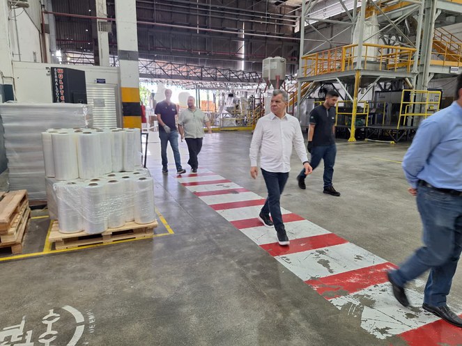 Foto mostra homens andando numa fábrica de plásticos