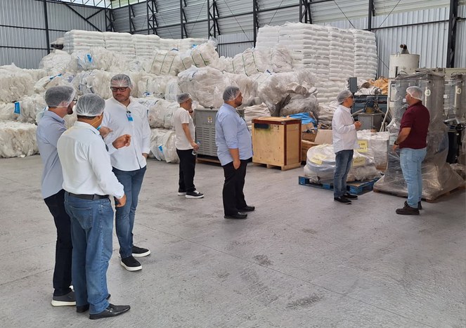 Foto mostra grupo de pessoas com touca na cabeça em visita uma fábrica de termoplástico