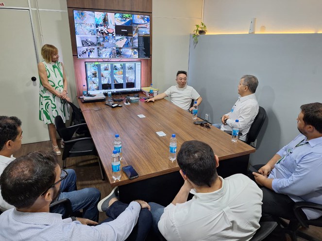 Foto mostra grupo de pessoas em uma reunião, com telões ao fundo