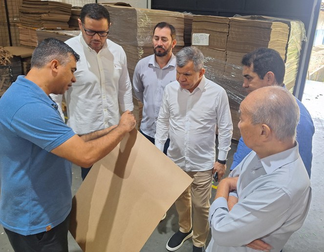 Foto mostra homem de blusa azul mostrando papelão a um grupo de outros homens