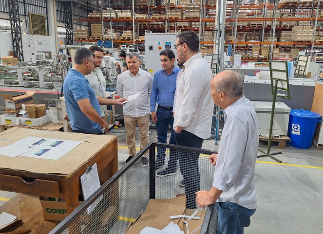 Foto mostra grupo de homens olhando para um papel que está na mão de homem com blusa azul