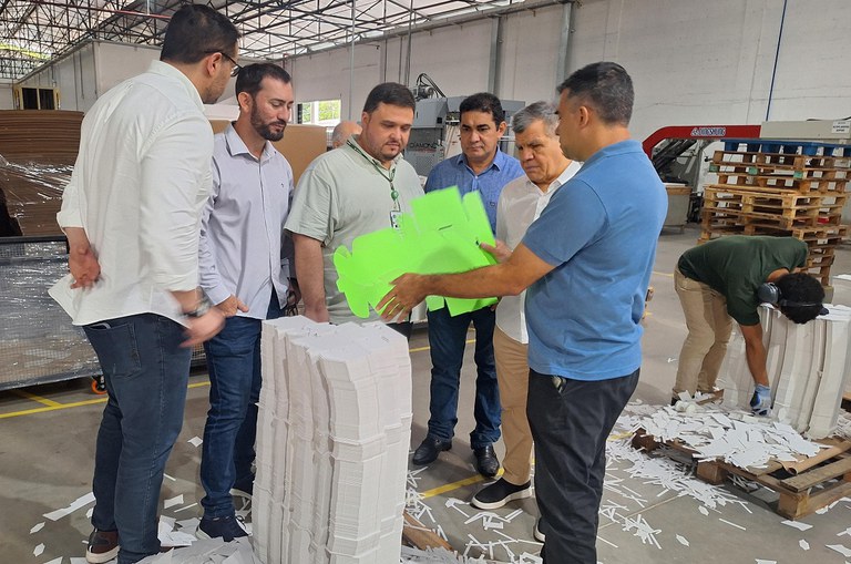Foto mostra homem de blusa azul mostrando papelão verde a outros homens