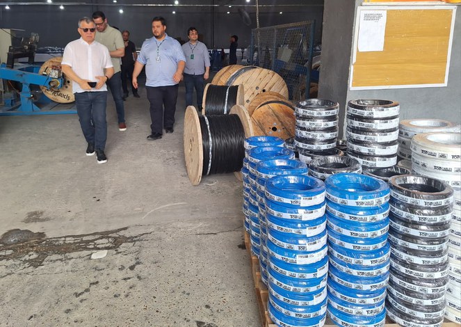 Foto mostra homens caminhando ao lado de pacotes de fios elétricos