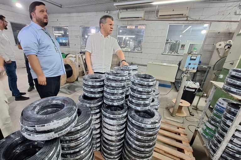 Foto mostra dois homens próximos a pacotes de fios elétricos