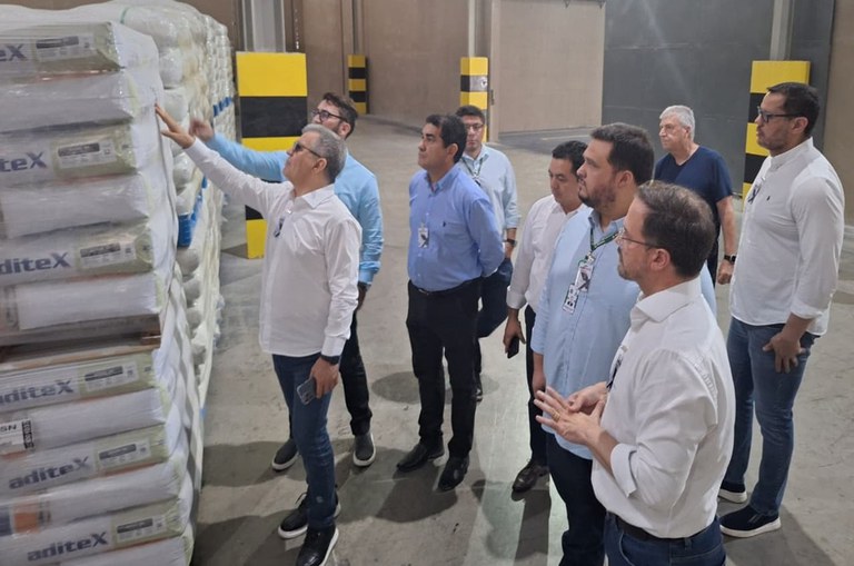 Foto mostra homem de blusa branco tocando em sacos brancos, observados por outros homens