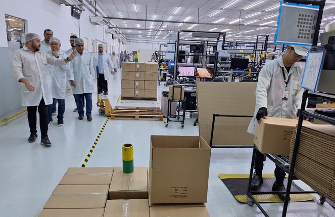 Foto mostra homens de bata caminhando ao lado de equipamentos e caixas de papel