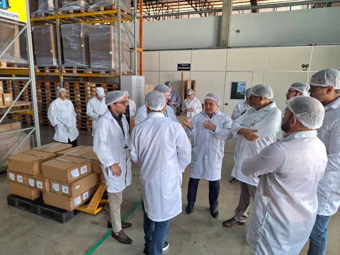 Foto mostra homens de bata conversando num depósito de caixas