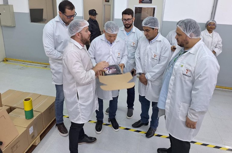 Foto mostra grupo de pessoas vestidas com bata e olhando para uma caixa