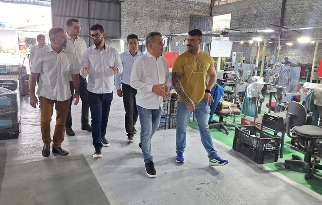 Foto mostra grupo de pessoas caminhando dentro de uma fábrica de peças para fabricação de automóveis