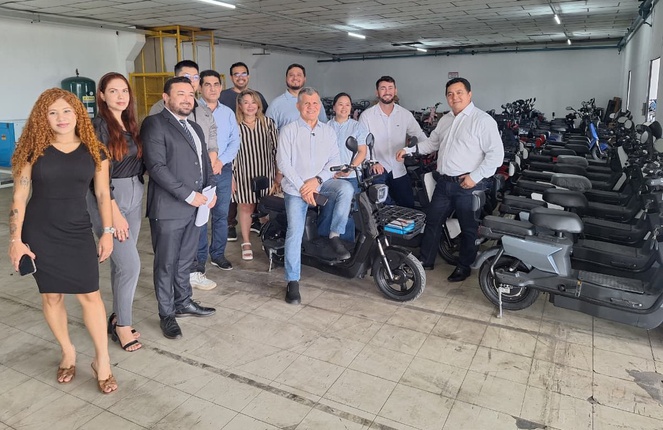 Foto mostra homem sentado em uma moto ao lado de grupo de pessoas e de outras motocicletas