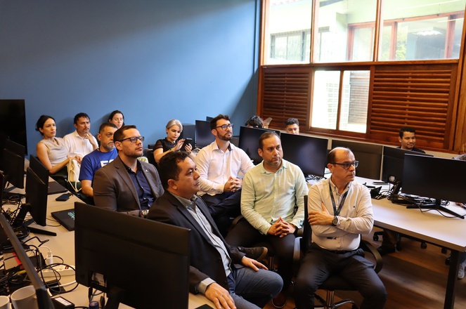 Foto mostra pessoas olhando para uma apresentação