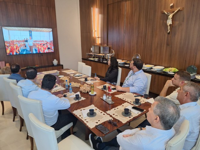 Foto mostra pessoas em reunião com apoio de um telão