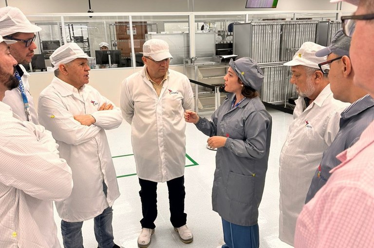 Foto mostra mulher fazendo uma explicação para um grupo de homens; todos com touca e jaleco